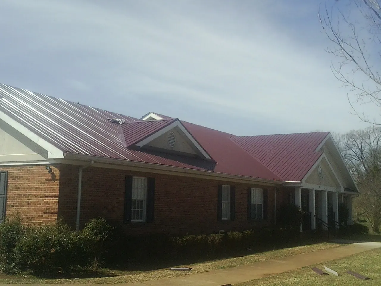 Red metal roof with gabled entries on a long brick building, from a Hail Damage Roof Repair job in Stratton