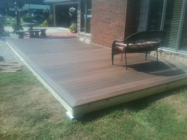 New wood deck and wicker chair beside a brick house in Stratton